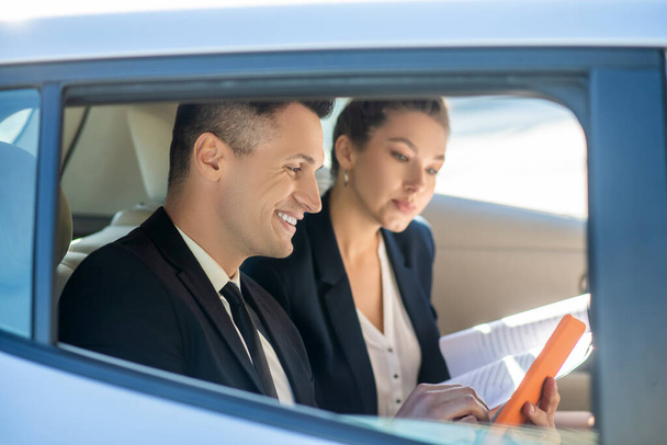Attractive man with tablet and attentive woman with documents in car - Photo, Image