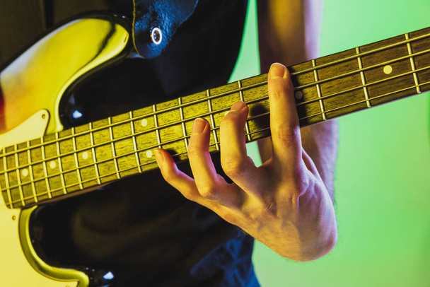 Close up musician hands playing bass guitar on gradient studio background in neon light - Foto, afbeelding
