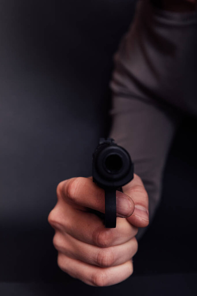 Männliche Hand mit Pistole isoliert auf schwarzem Hintergrund. Mann mit schussbereiter Waffe konzentriert sich auf Waffe. - Foto, Bild