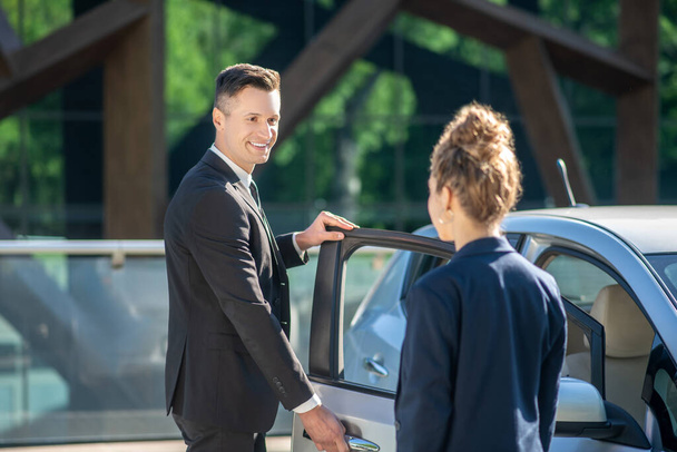 Man in suit opening door to car, woman standing with back - Foto, Imagen