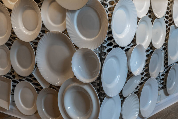 Black and white photography of white crockery plates and dishes are displayed on white lattice wall. Dinnerware of different sizes - Photo, Image