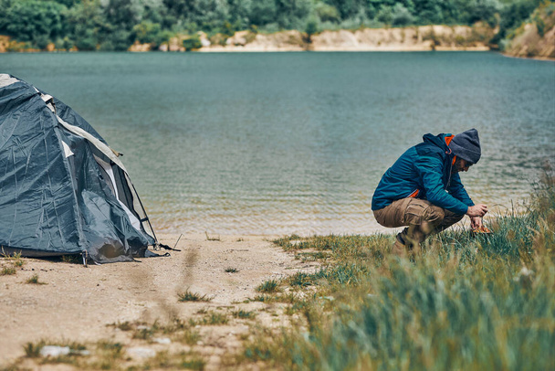 Side view of young attractive bearded man preparing lunch on camping trip. Weekend activities concept. - Photo, Image