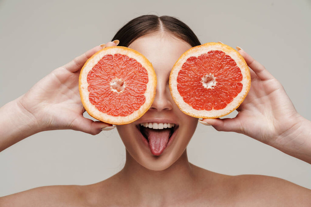 Image of cheerful nice shirtless woman smiling while making fun with grapefruit isolated over grey background - Foto, immagini