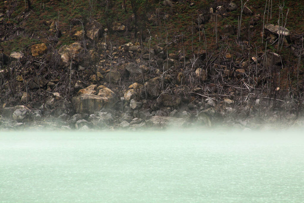 La niebla se evapora en el lago del volcán Kawah Putih, cerca de Bandung, Indonesia. Es un lago sulfúrico situado en el cráter volcánico en la zona montañosa de Ciwidey, cerca de Bandung, Java Occidental en Indonesia
. - Foto, Imagen
