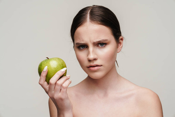 Image of beautiful displeased shirtless woman posing with green apple isolated over grey background - Fotografie, Obrázek