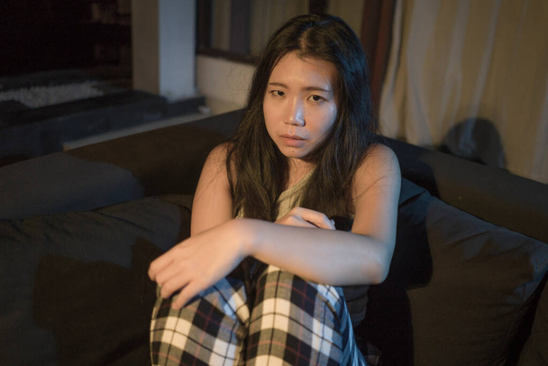 dramatic home lifestyle portrait of young beautiful sad and depressed Asian Korean woman lying in pain at living room sofa couch broken heart suffering depression and anxiety - Foto, Bild