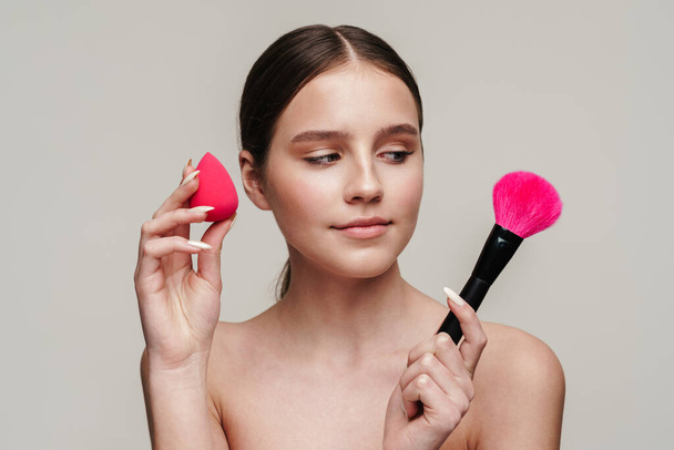 Image of beautiful young shirtless woman using makeup sponge and brush isolated over grey background - Zdjęcie, obraz