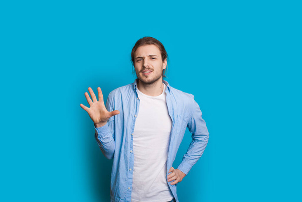 Caucasian man with long hair and beard gesturing number 5 with palm while posing on a blue studio wall - Photo, Image