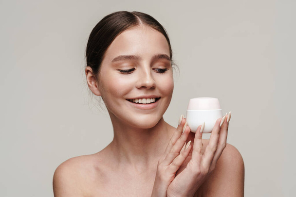 Image of pleased young shirtless woman showing face cream and smiling isolated over grey background - Foto, immagini