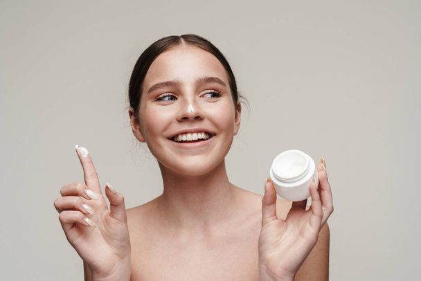 Image of pleased young shirtless woman showing face cream and laughing isolated over grey background - Foto, immagini