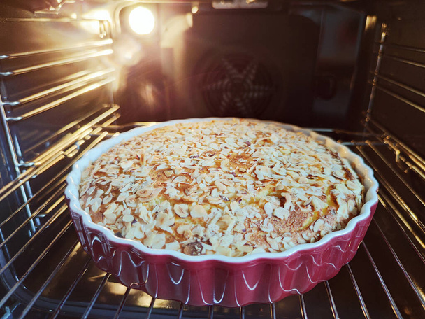 Fresh baked golden apple pie in red dish in hot oven at cozy kitchen - Photo, image