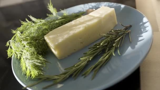 Close up of cheese and greenery on a glass plate. Stock footage. Delicious cheese with fresh green dill and rosemary, food and french ciusine concept. - Imágenes, Vídeo