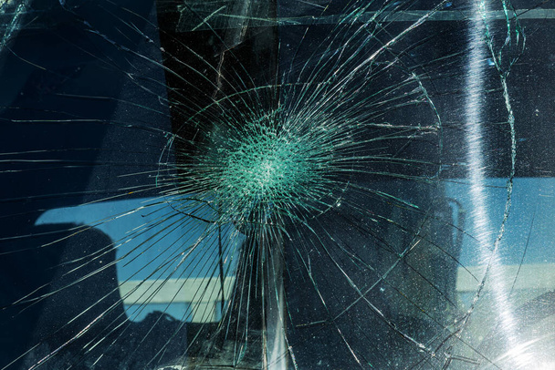 壊れた車のフロントガラス。放射状の亀裂のウェブ、トリプルフロントガラスに亀裂。壊れたフロントガラス車、道路上の対向石の痕跡や道路上の歩行者や動物の痕跡を持つ破損したガラス - 写真・画像