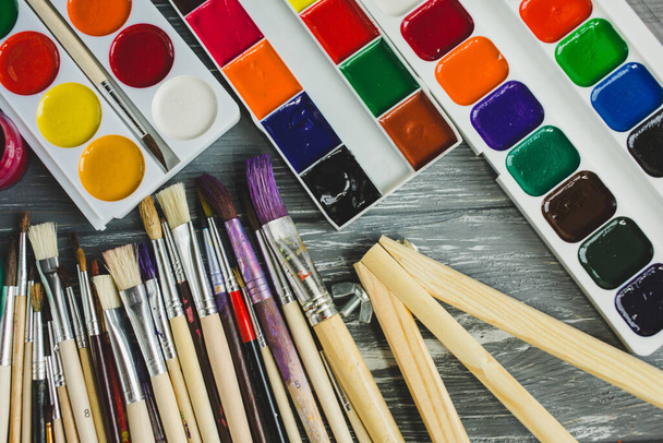 Close-up de pincéis de pintura artista, paleta e aquarelas no fundo de madeira cinza grunge. Conjunto de tintas multicoloridas. - Foto, Imagem