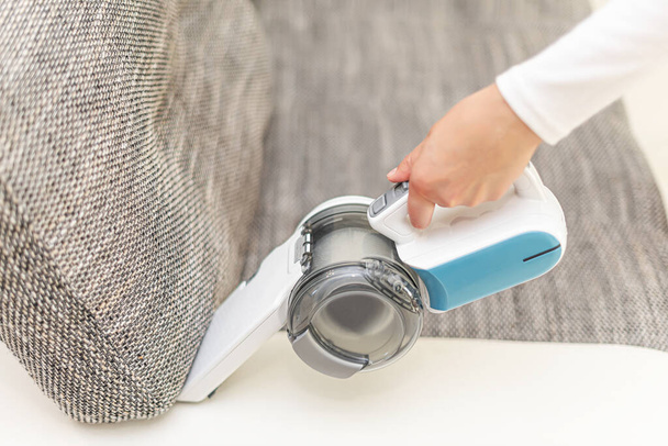 Woman vacuuming furniture in a house with a hand-held portable vacuum cleaner. - Foto, Imagem