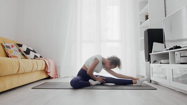Slanke sportieve Afro-Amerikaanse vrouw die yoga beoefent op een mat. Vrouw zit op fitness mat en strekt zich uit - Foto, afbeelding