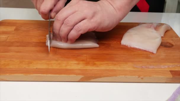 Un hombre corta un filete de calamar con un cuchillo en un tablero de cocina de madera, manos, primer plano
 - Metraje, vídeo