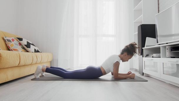 Тонкая спортивная американка из Африки, практикующая йогу на коврике. Женщина в активной одежде выполнять упражнения положение доски на мат
 - Фото, изображение