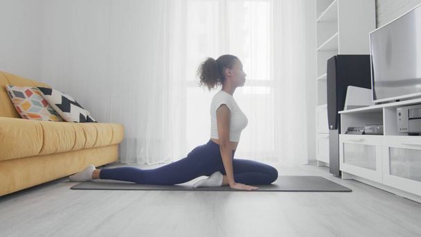 Тонка спортивна афроамериканка практикує йогу на килимку. Молода жінка робить тренування йоги в кімнаті
 - Фото, зображення