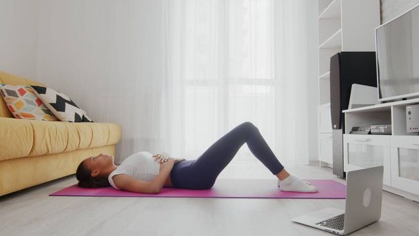 On-line home work out woman using internet services with help of her instructor on laptop at home. Slim sporty african american woman practicing yoga on a mat. Woman having a rest after training - Photo, Image
