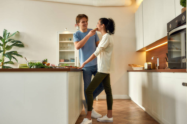 Eat healthy. Full length shot of happy couple, vegetarians cooking breakfast in the kitchen. Woman tasting sandwich that they made together. Vegetarianism, healthy food, diet, stay home concept - Foto, immagini