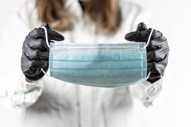 Jonge vrouwelijke arts zet medische masker met zwarte handschoenen met toga op, concept van de geneeskunde en persoonlijke bescherming. Koolvis. - Foto, afbeelding