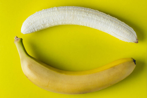 Dva banány na žlutém pozadí. Jeden banán se oloupal. Fotka shora. Banán jako pozadí - Fotografie, Obrázek