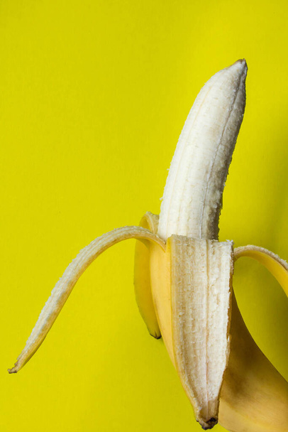 Obierany banan na żółtym tle. Kreatywne zdjęcie banana. Banan jako tło. - Zdjęcie, obraz
