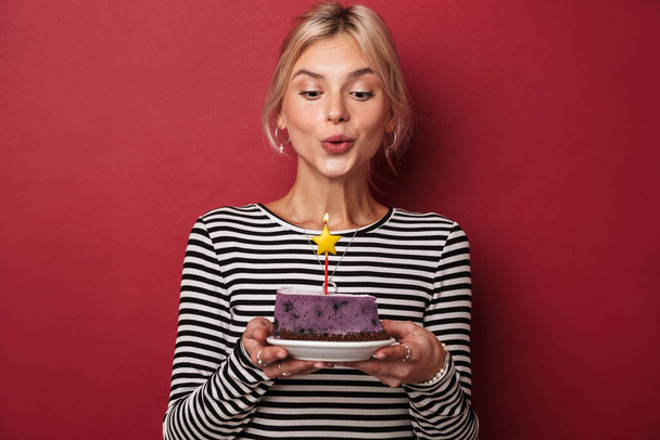 Εικόνα του ωραία ευτυχισμένη γυναίκα σε ριγέ φούτερ κρατώντας τούρτα με κερί απομονώνονται σε κόκκινο φόντο - Φωτογραφία, εικόνα