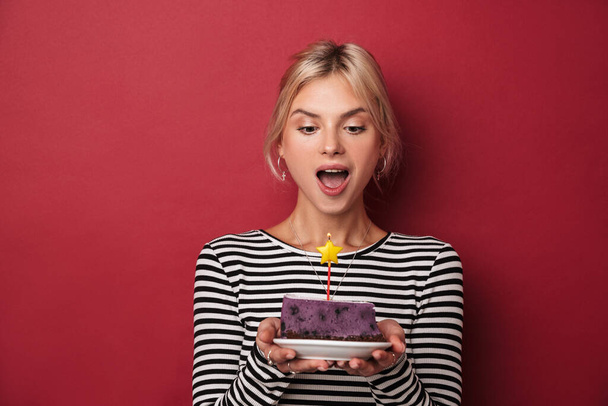 Image of nice delighted woman in striped sweatshirt holding cake with candle isolated over red background - Φωτογραφία, εικόνα