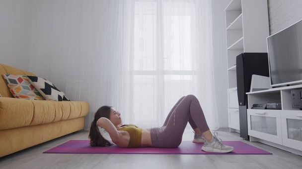 Portrait of a beautiful slim sporty woman practicing yoga on a mat. Woman doing abs workout at home - Photo, Image