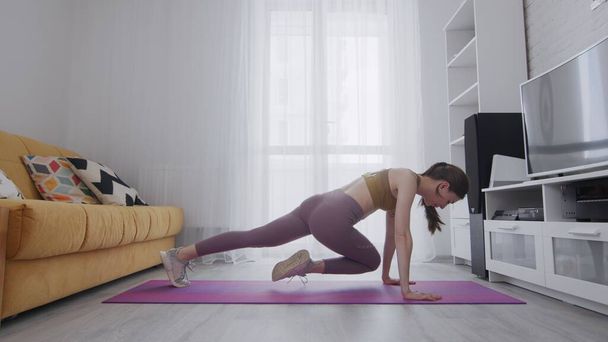 Portret pięknej szczupłej, wysportowanej kobiety ćwiczącej jogę na macie. Kobieta robi ćwiczenia sportowe wspinaczka w domu - Zdjęcie, obraz