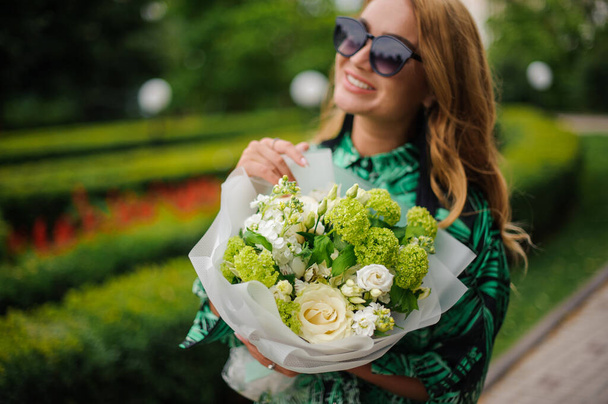 Close-up of smiling woman holds bouquet with white roses and green hydrangea. - Photo, Image