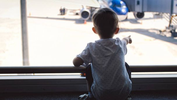 Kleiner Junge zeigt mit Finger auf Flugzeug am Flughafen - Foto, Bild