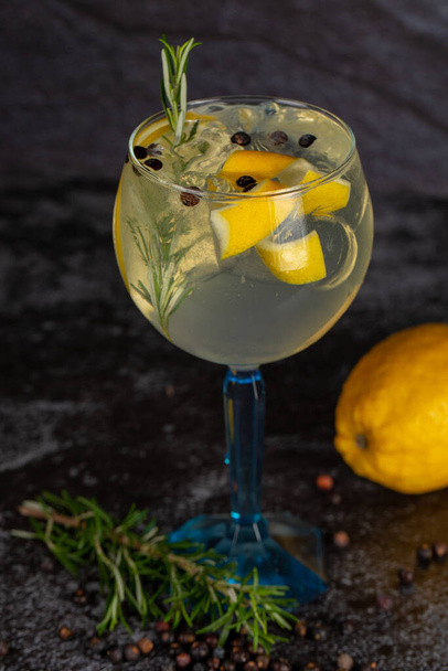 Alcoholic drink gin and tonic cocktail with lemon, rosemary, pepper and ice on concrete background. space for text. - Photo, Image