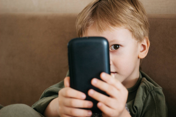 Little beautiful boy uses a phone, Caucasian boy hold smartphone - Fotografie, Obrázek