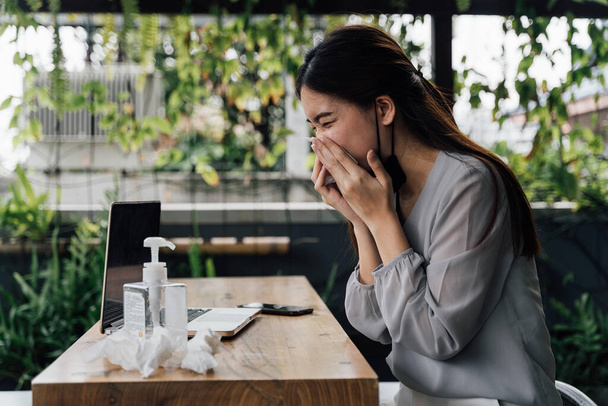 One 20s young adult business woman sneezing with tissue handkerchief. Casual female freelancer working with laptop outdoors with alcohol gel on desk. With copy space - Photo, Image