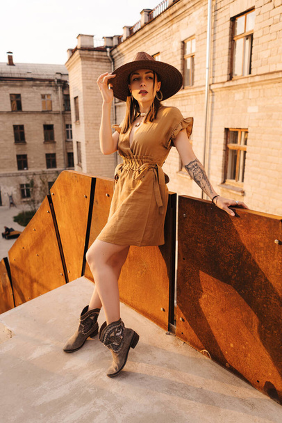 Mladá módní dívka oblečená v letních šatech s proutěný široký klobouk chodí a pózuje ve starém městě - Fotografie, Obrázek