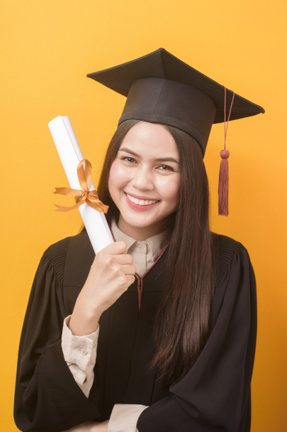 Portrait of happy Beautiful woman in graduation gown is holding education certificate on yellow background  - Fotó, kép