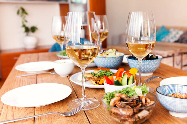 Vysoký úhel dřevěného stolu servírované s různými domácími pokrmy a sklenicemi s vínem v útulném obývacím pokoji doma - Fotografie, Obrázek