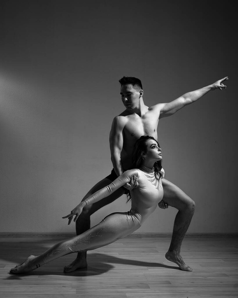 A man and a woman are dancing modern ballet. Acrobatic couple perform number on a white background. A duet of gymnasts rehearsing a performance with support. Monochrome photo. - Foto, immagini