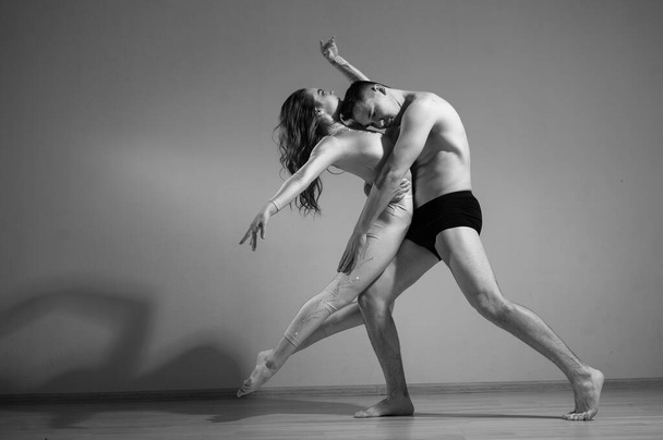 A man and a woman are dancing modern ballet. Acrobatic couple perform number on a white background. A duet of gymnasts rehearsing a performance with support. Monochrome photo. - Photo, image