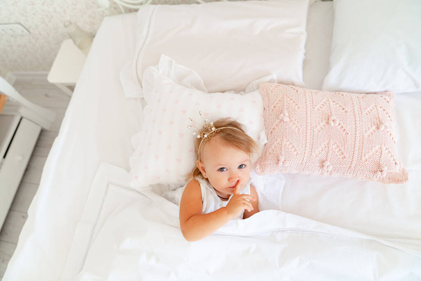 little girl sleeping in bed in bedroom with crown. Princess birthday party.  - 写真・画像