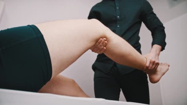 Junger Mann lässt sein Knie vom Spezialisten untersuchen. Physiotherapie Knie Flexibilität - Filmmaterial, Video