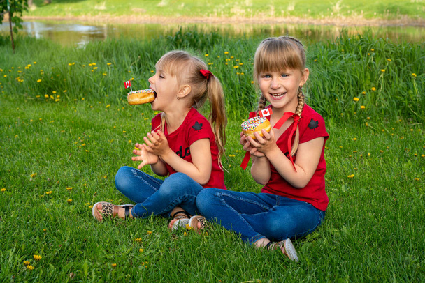 Feliz Día de Canadá Concepto de Celebración. Dos chicas caucásicas con rosquillas celebrando fuera de Canadian Anniverasy
. - Foto, Imagen