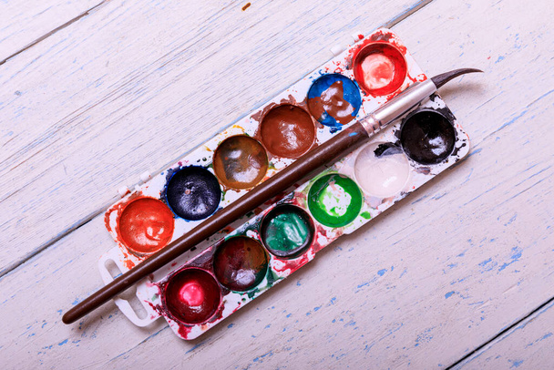 Профессиональные акварельные краски в коробке с кисточками на старой белой доске
 - Фото, изображение