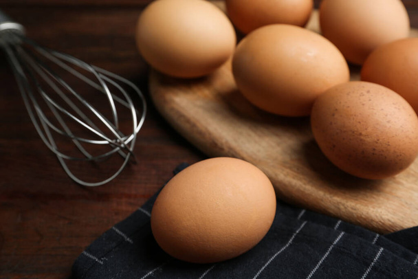 Chicken eggs and whisk on wooden table, closeup - Fotoğraf, Görsel