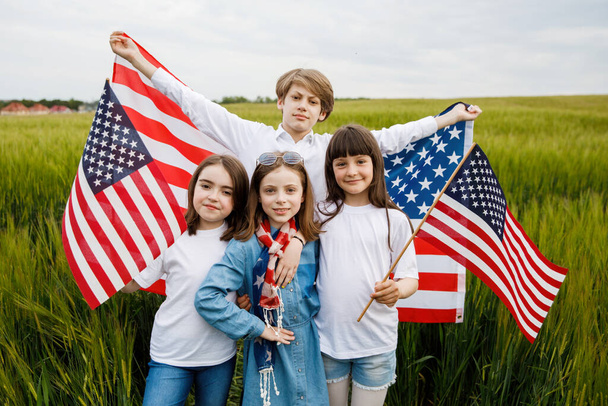 Czworo wesołych dzieci stoi na polu z amerykańską flagą w rękach. - Zdjęcie, obraz