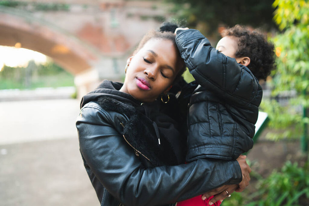 Портрет африканської матері з сином стоїть на відкритому повітрі в парку, розважаючись. Монастирська родина. - Фото, зображення