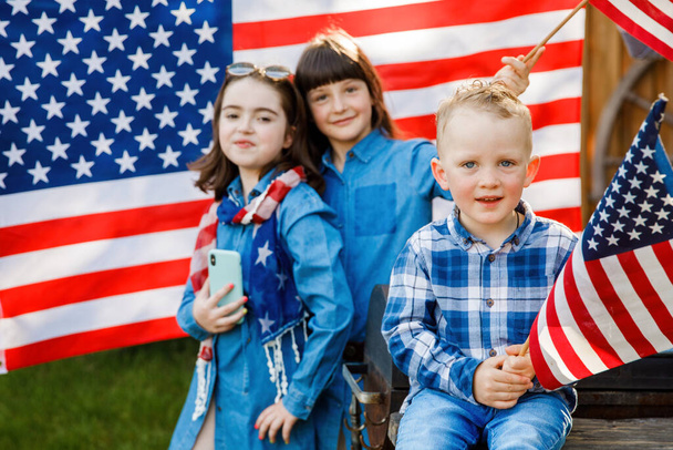 Lindo chico rubio y dos chicas se divierten en la calle en el fondo de la bandera estadounidense
 - Foto, imagen